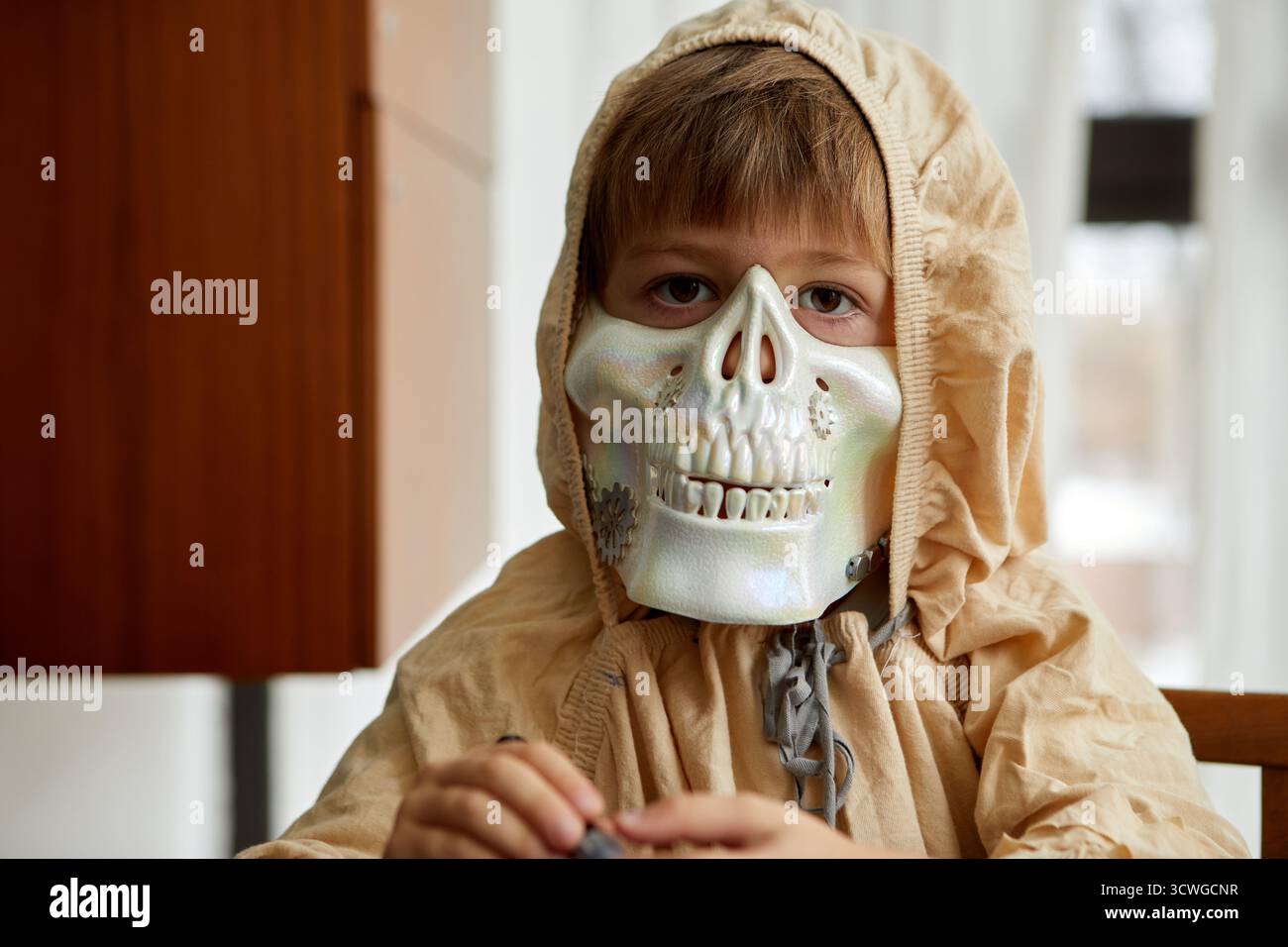 Un enfant portant un masque squelette effrayant avec une capuche confortable est tout prêt pour un peu de plaisir d'Halloween à l'intérieur Banque D'Images Un enfant portant un masque squelette effrayant avec une capuche confortable est tout prêt pour un peu de plaisir d'Halloween à l'intérieur Banque D'Images