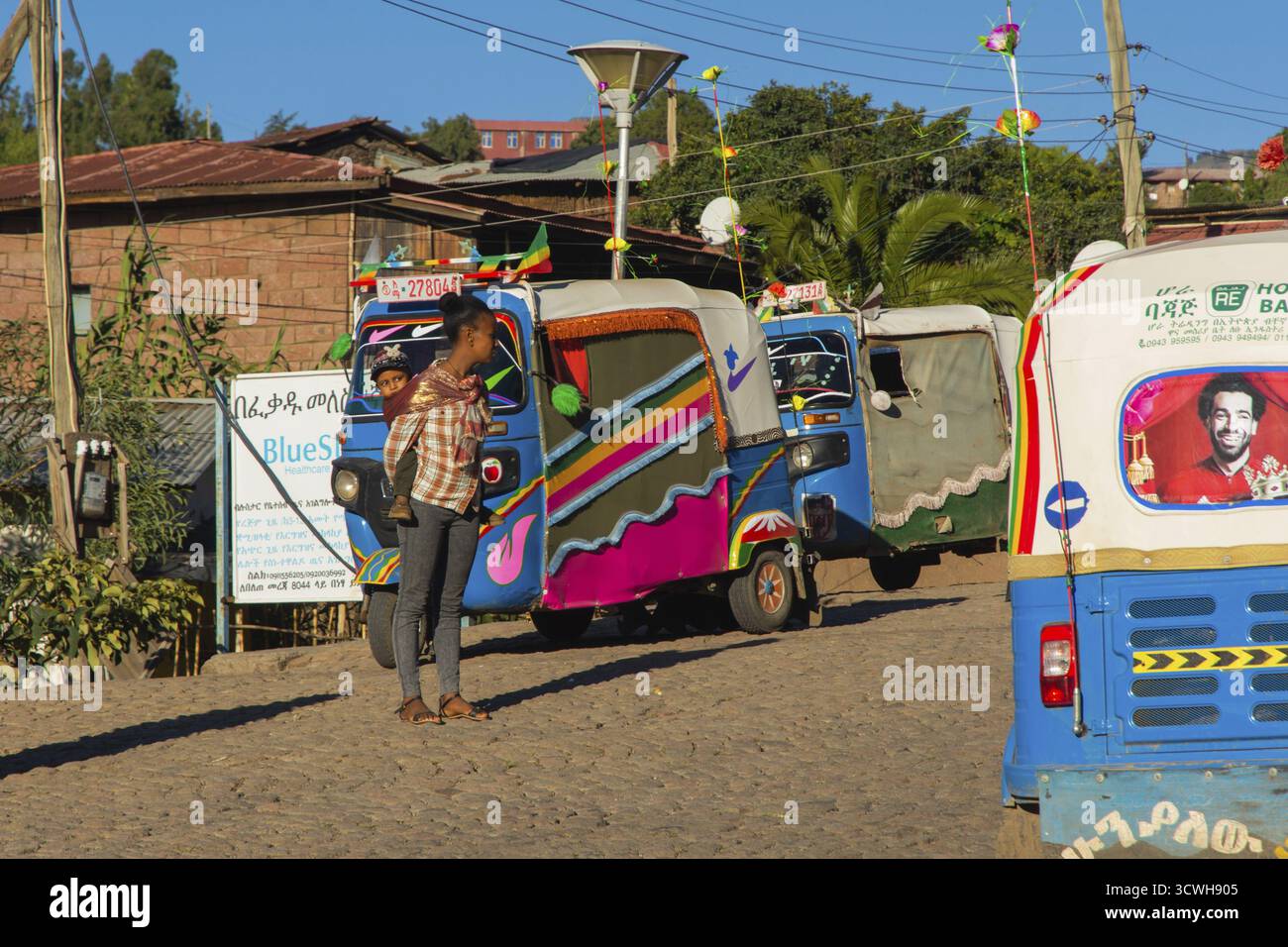 Lalibela, Ethiopie - Nov 2018: Femme transportant un enfant à l'arrière entre les remorqueurs de tuk à Lalibela, Ethiopie Banque D'Images