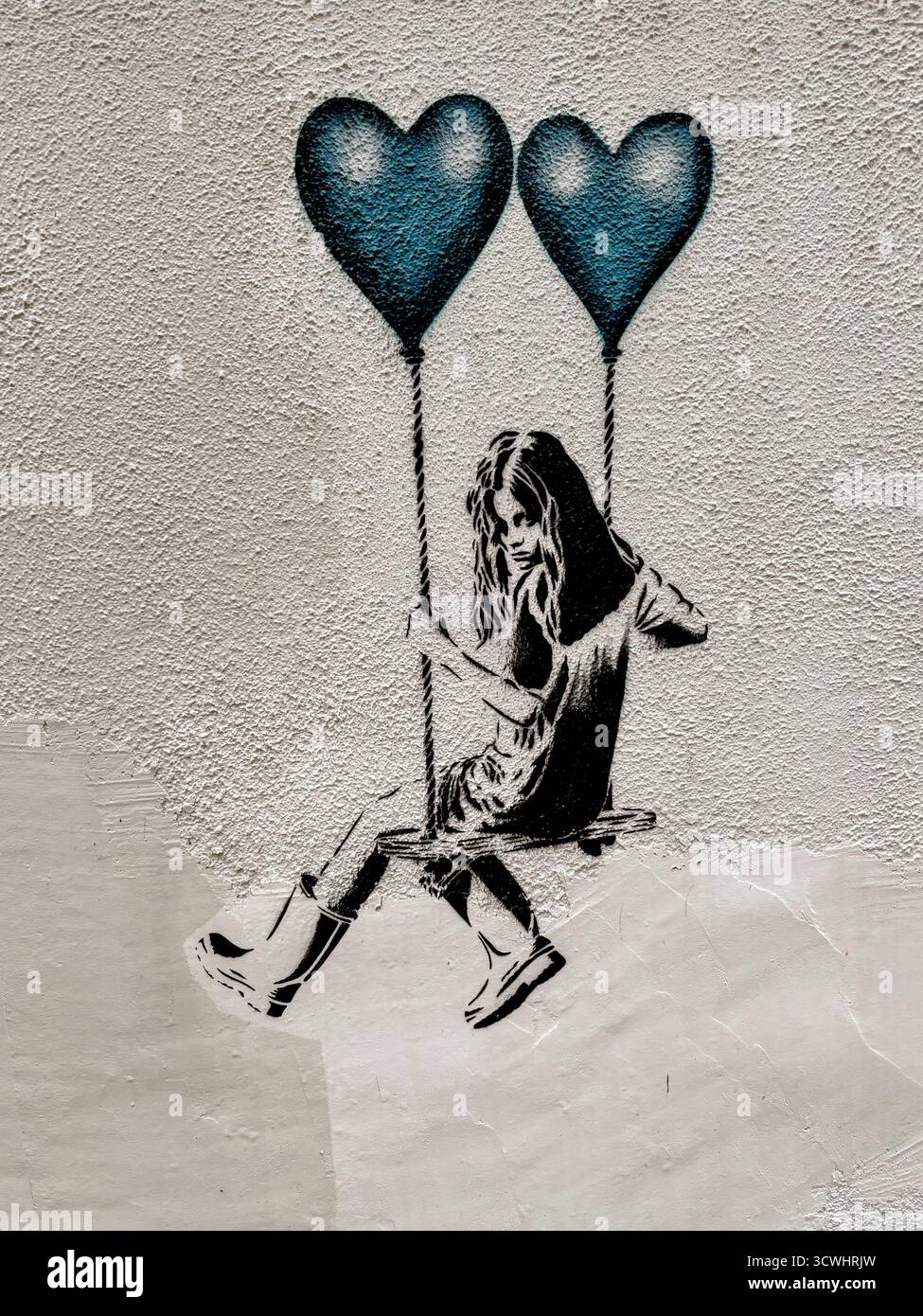Pochoir graffiti d'une fille sur une balançoire tenue par deux ballons Blue Heart Banque D'Images