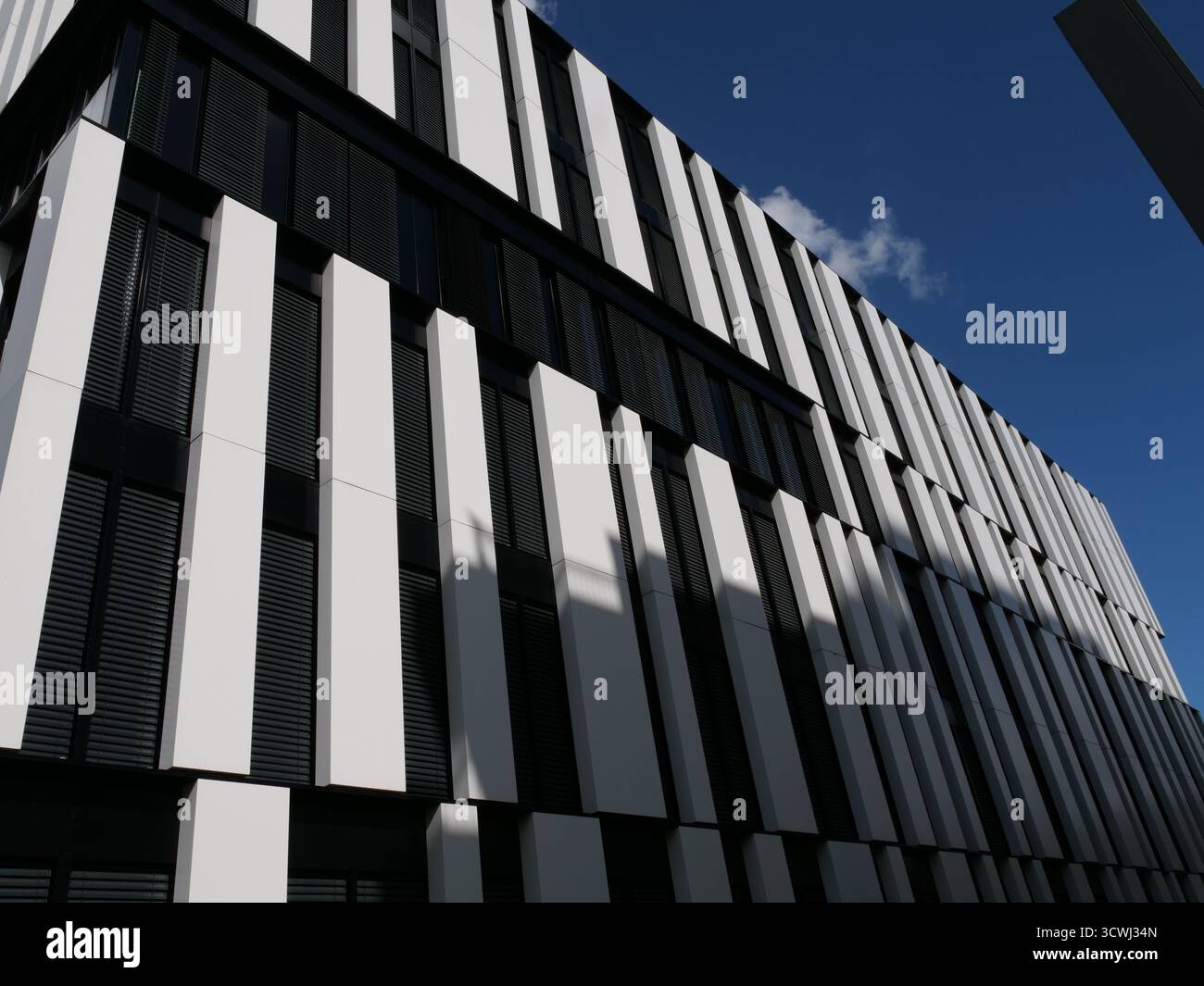 Façade moderne d'immeuble de bureaux avec panneaux blancs verticaux et lattes de fenêtre noires, architecture géométrique, vue en angle bas, ciel bleu clair, lumière et Sha Banque D'Images
