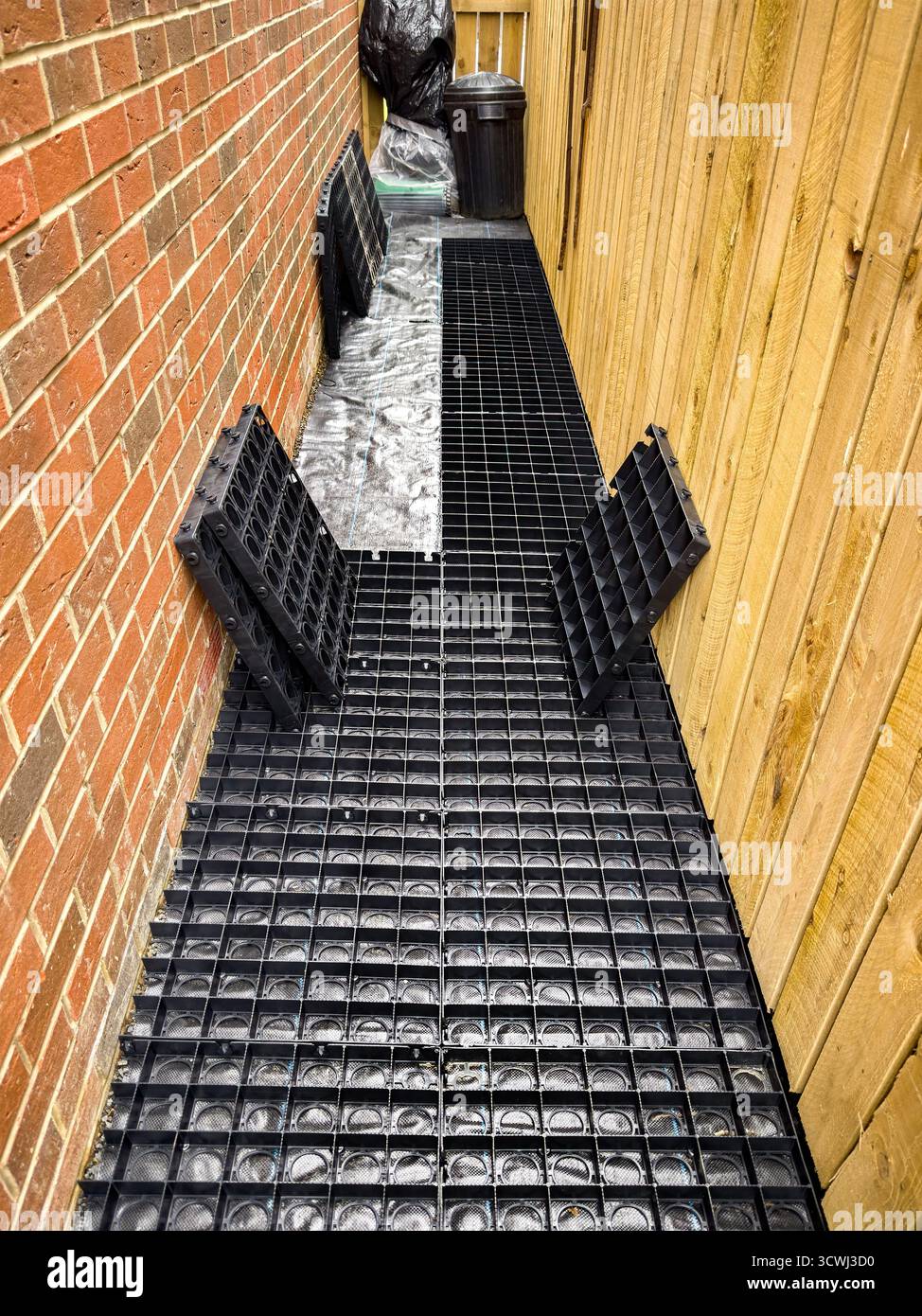 Espace extérieur étroit avec des grilles de drainage noires posées entre le mur de briques et la clôture en bois - Image de stock capturée avec un smartphone