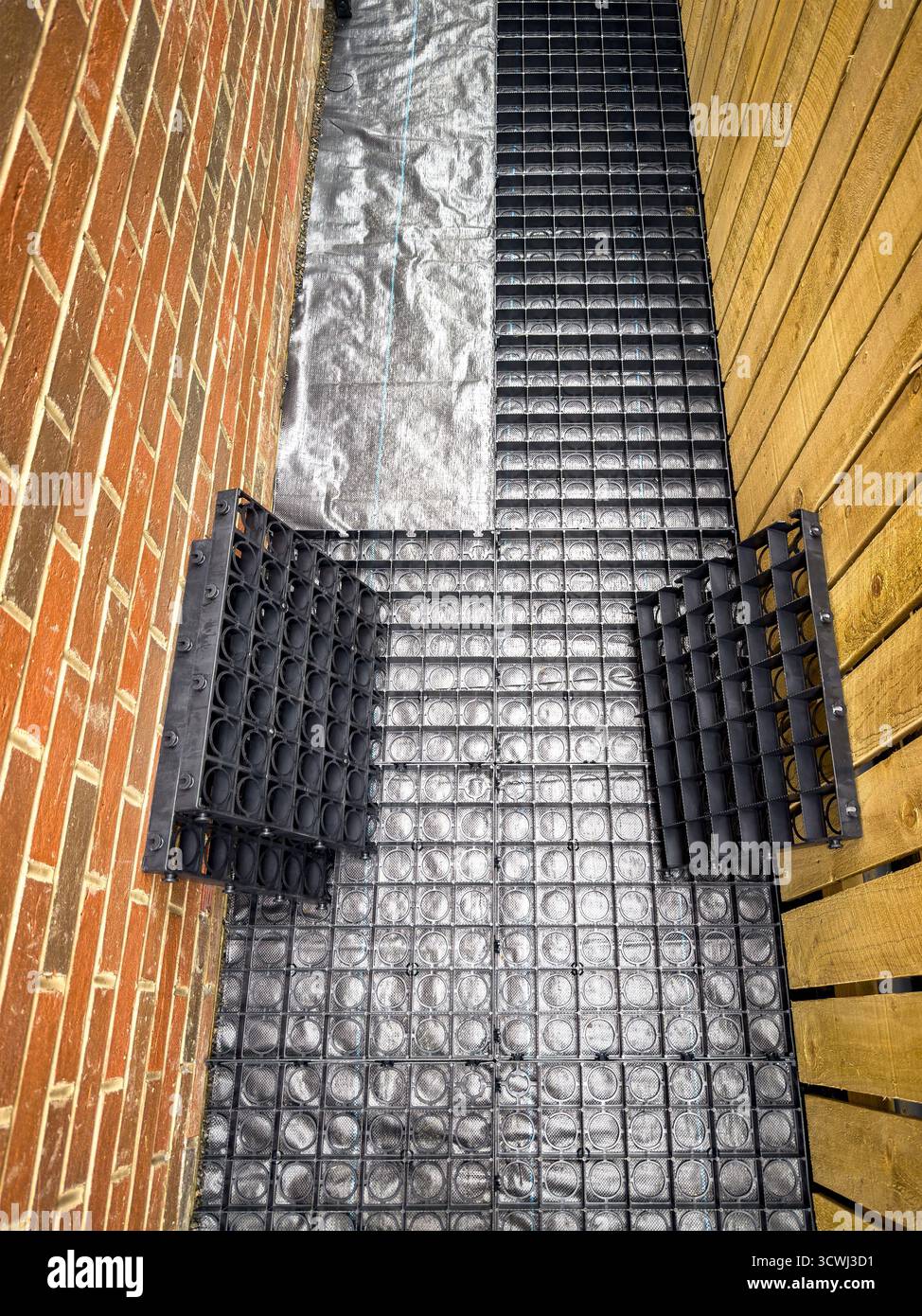 Espace extérieur étroit avec des grilles de drainage noires posées entre le mur de briques et la clôture en bois - Image de stock capturée avec un smartphone