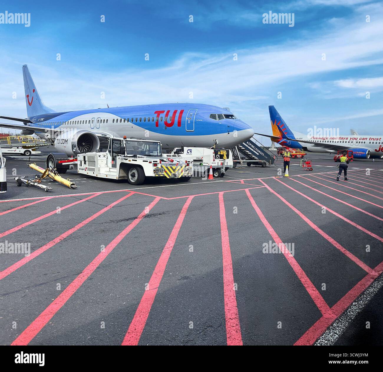 Avion TUI sur le tarmac d'un aéroport desservi par une équipe au sol avec un ciel bleu clair en arrière-plan Banque D'Images