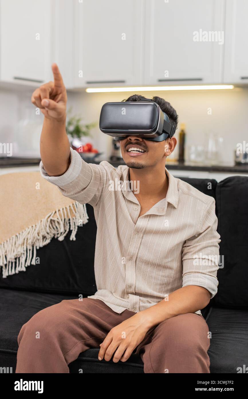 L'homme indien à la maison porte un casque VR dit wow regarde des films et explore le cinéma virtuel avec intérêt. Arabian Guy on sofa Views contenu en ligne dit des mots courts hoche la tête et maintient le mouvement de la tête calme Banque D'Images
