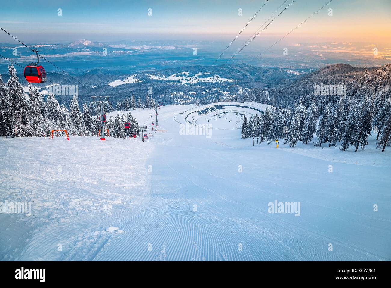 Piste de ski fraîchement entretenue et gondoles de ski au-dessus de la piste de ski au lever du soleil, Poiana Brasov, Roumanie, Europe Banque D'Images