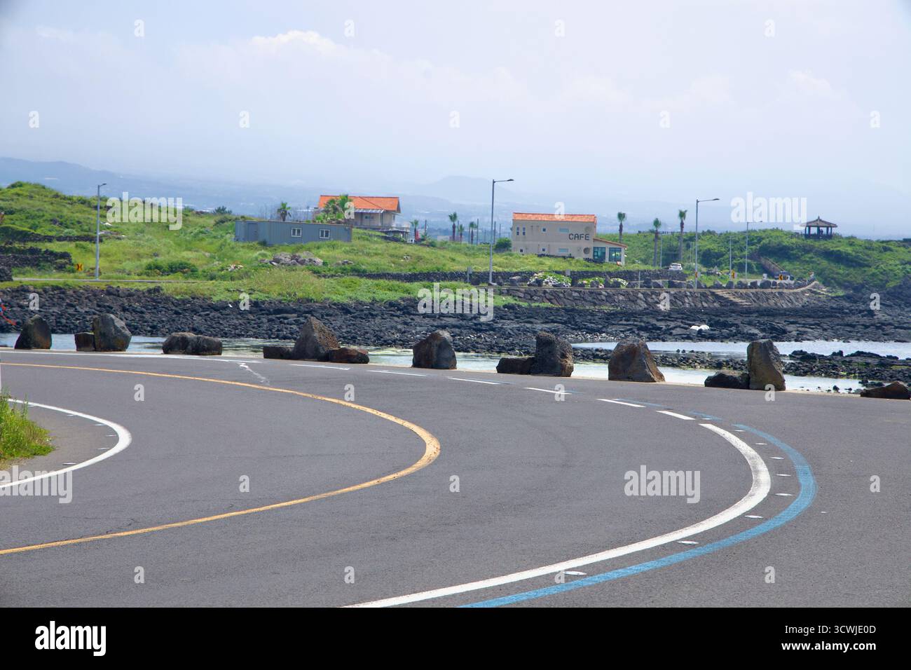 Une double courbe dans la route côtière passe des barrières de rochers et un petit café alors qu'elle longe des plates-marées et des récifs de lave près de Shinheung. Banque D'Images