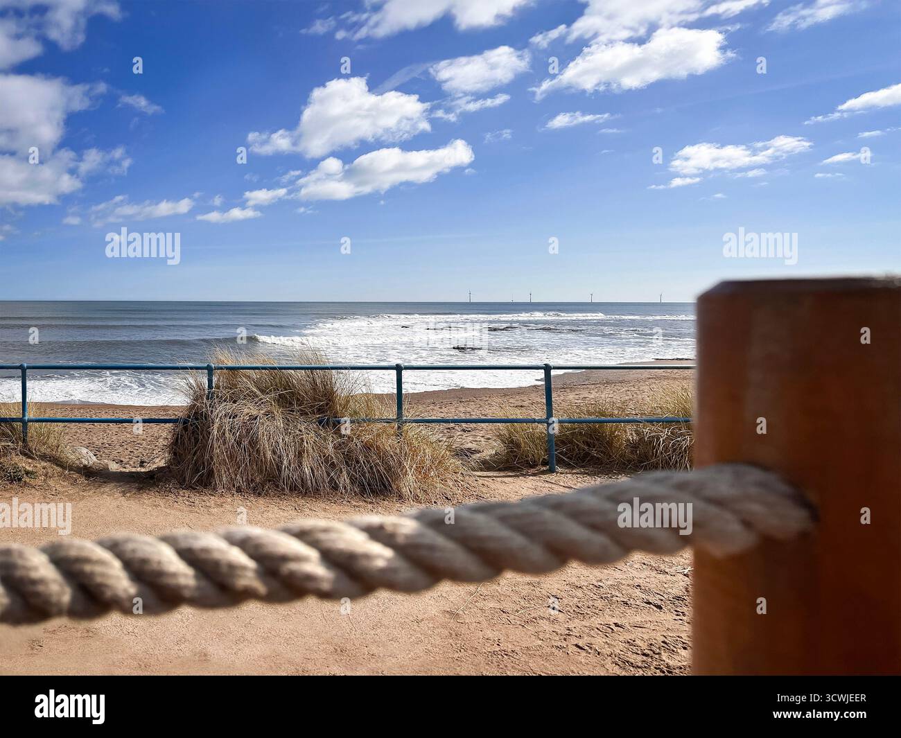 Vue sur la belle plage ensoleillée avec des dunes d'herbe, vagues de l'océan, balustrade, et le ciel partiellement nuageux au Needles eye café newbiggin northumberland uk Banque D'Images