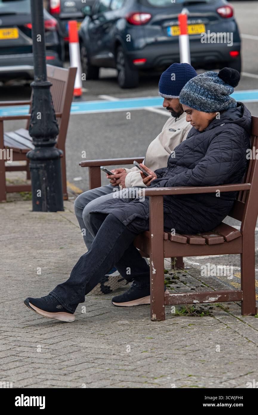 Deux hommes indiens ou asiatiques assis sur un banc en bois regardant les écrans de leurs smartphones. Banque D'Images