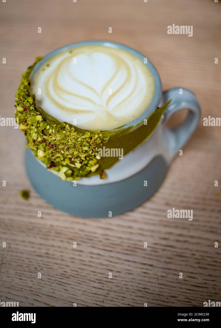 Latte Matcha avec latte art en forme de coeur et bord de pistache écrasé dans une tasse en céramique bleue Banque D'Images