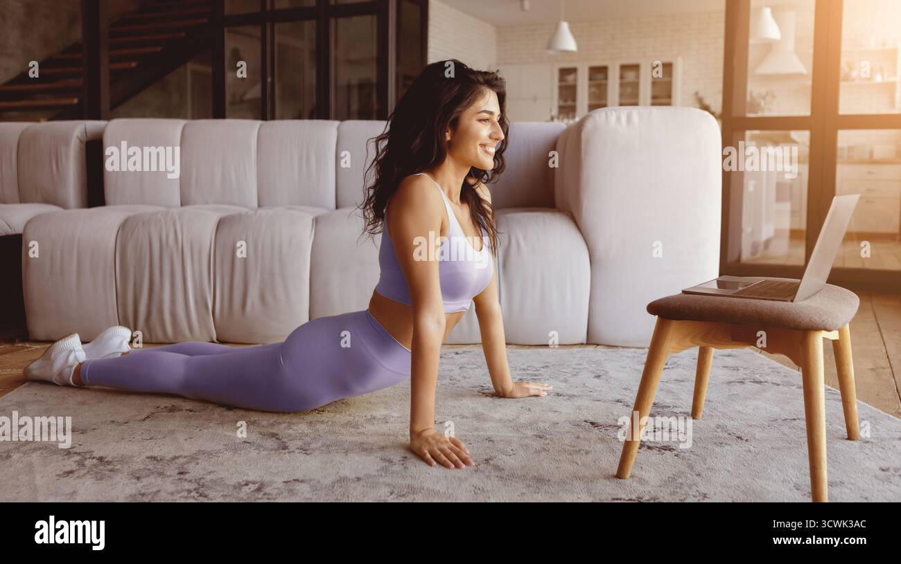 Femme pratiquant le yoga à la maison dans le salon lumineux avec ordinateur portable sur la chaise Banque D'Images