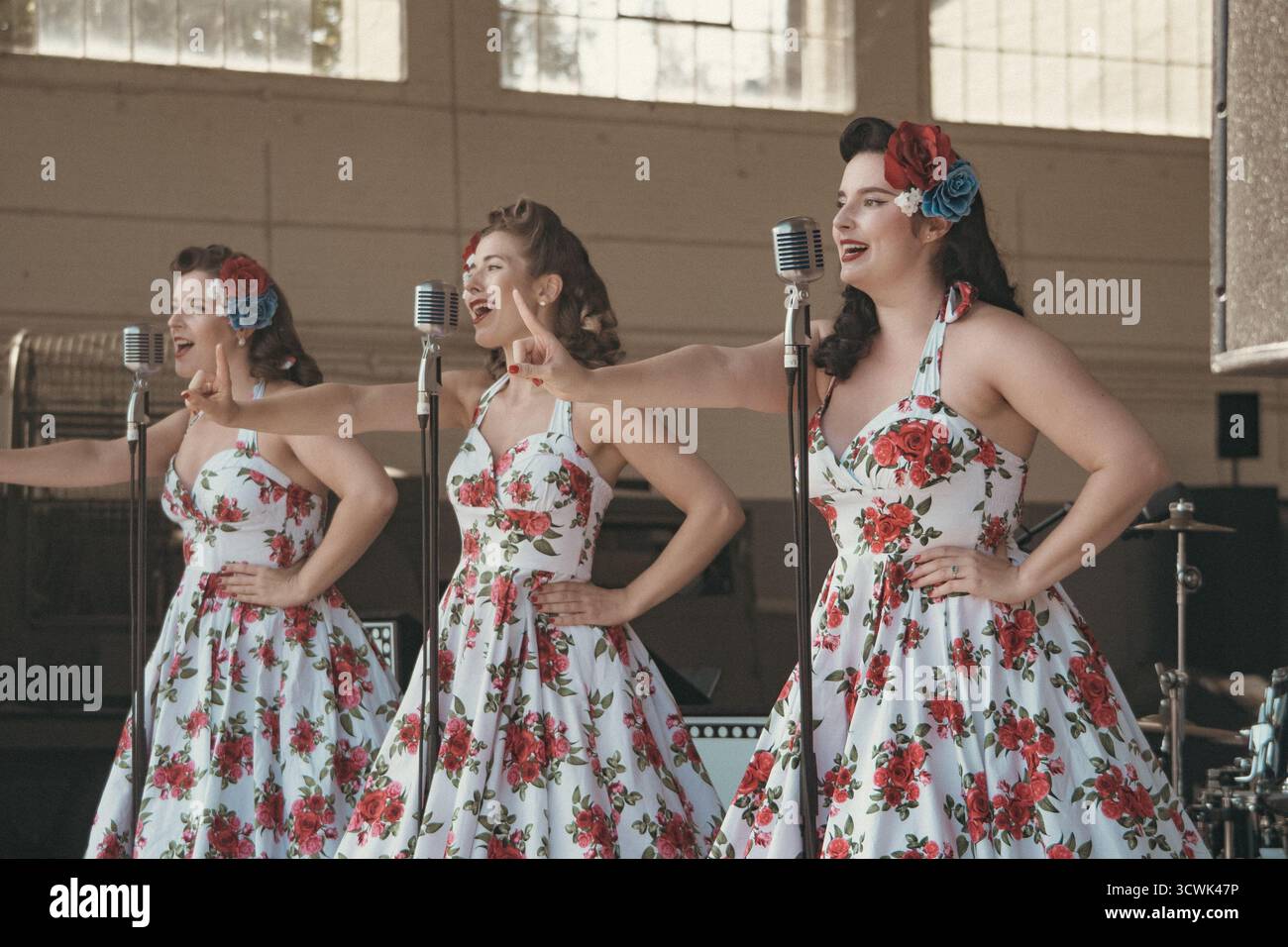 Trois artistes de style vintage dans des robes florales avec des microphones lors d'un événement de divertissement rétro Banque D'Images
