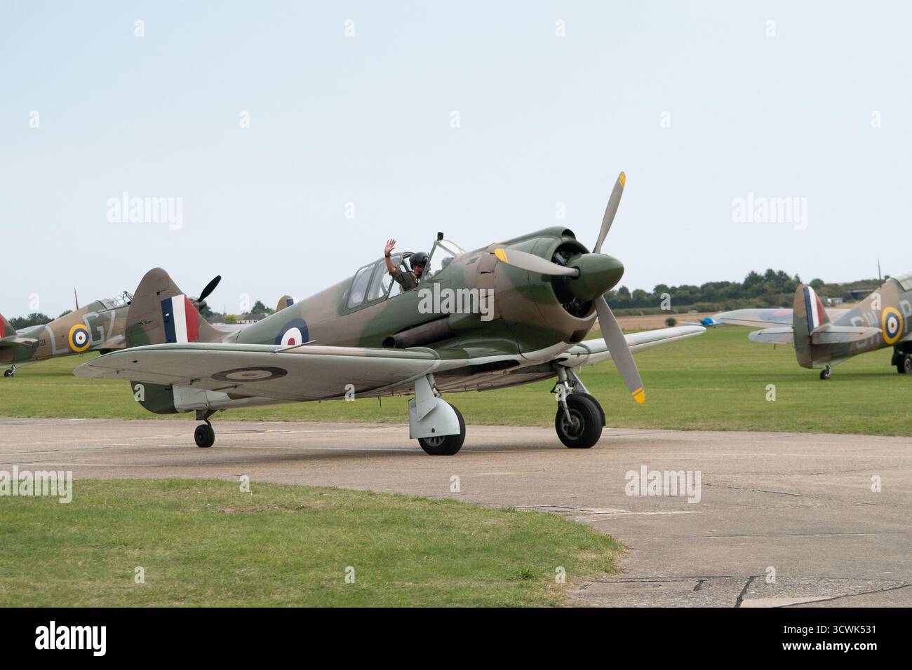 Avion de chasse Hawker Hurricane de la RAF avec pilote agitant à l'aérodrome de Duxford Banque D'Images