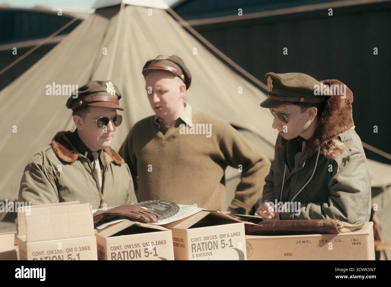 Trois officiers militaires en uniformes vintage discutant des rations à côté de tente en toile à l'aérodrome Banque D'Images