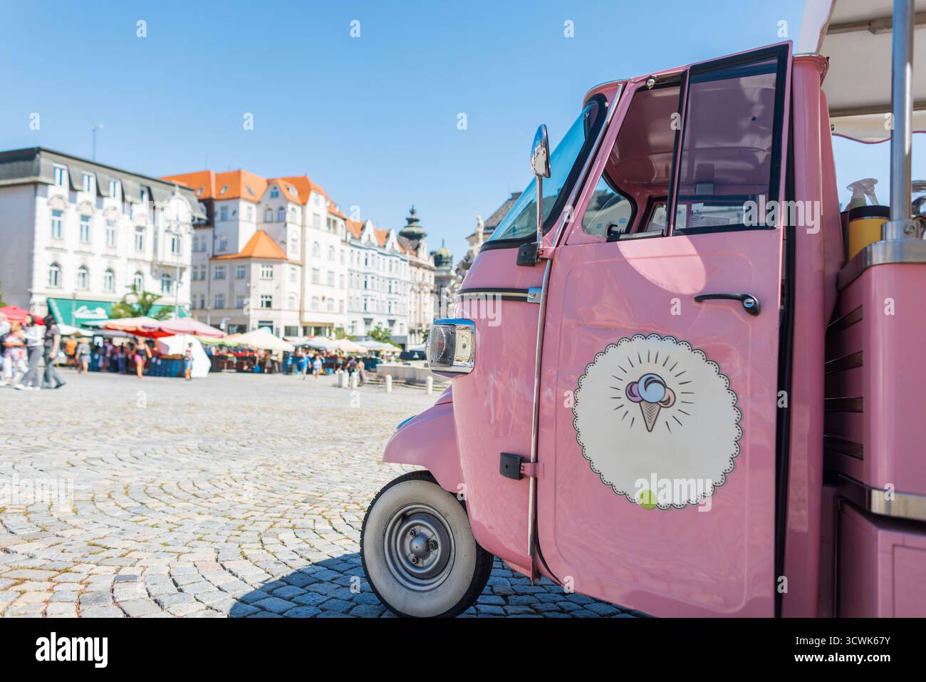 Camion de crème glacée rose garé sur Une place ensoleillée à Brno, République tchèque. Marché de rue coloré et bâtiments historiques en arrière-plan créez Un cheerf Banque D'Images