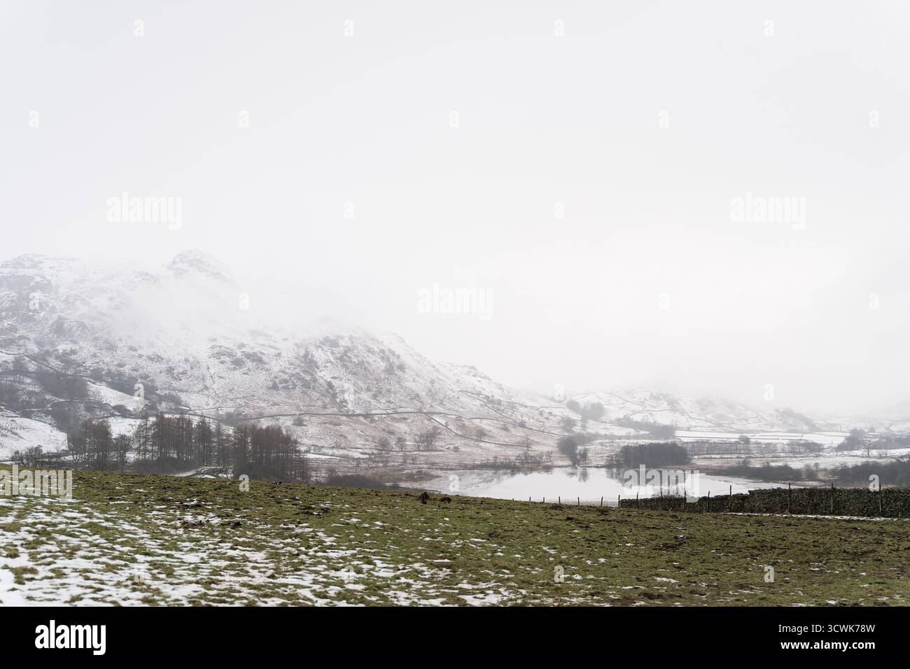 Des puits enneigés et un lac brumeux dans le paysage hivernal du Lake District Banque D'Images