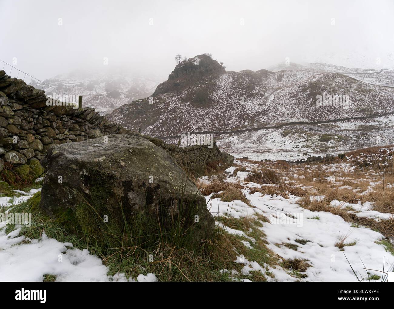 Des puits enneigés et un mur de pierre sèche dans le paysage hivernal du Lake District avec une atmosphère brumeuse Banque D'Images