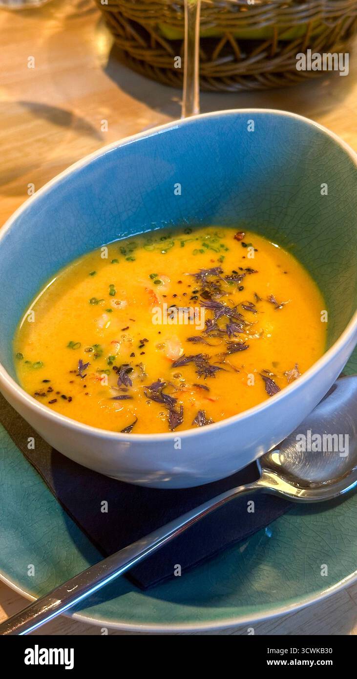 Grande assiette profonde avec soupe à la crème de citrouille saupoudrée d'épices et de pétales de bleuet dans un petit café maison Banque D'Images