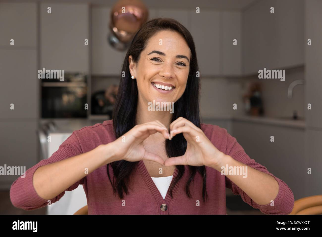 Positive joyeuse femme latine des années 30 joignant les doigts en forme de coeur Banque D'Images