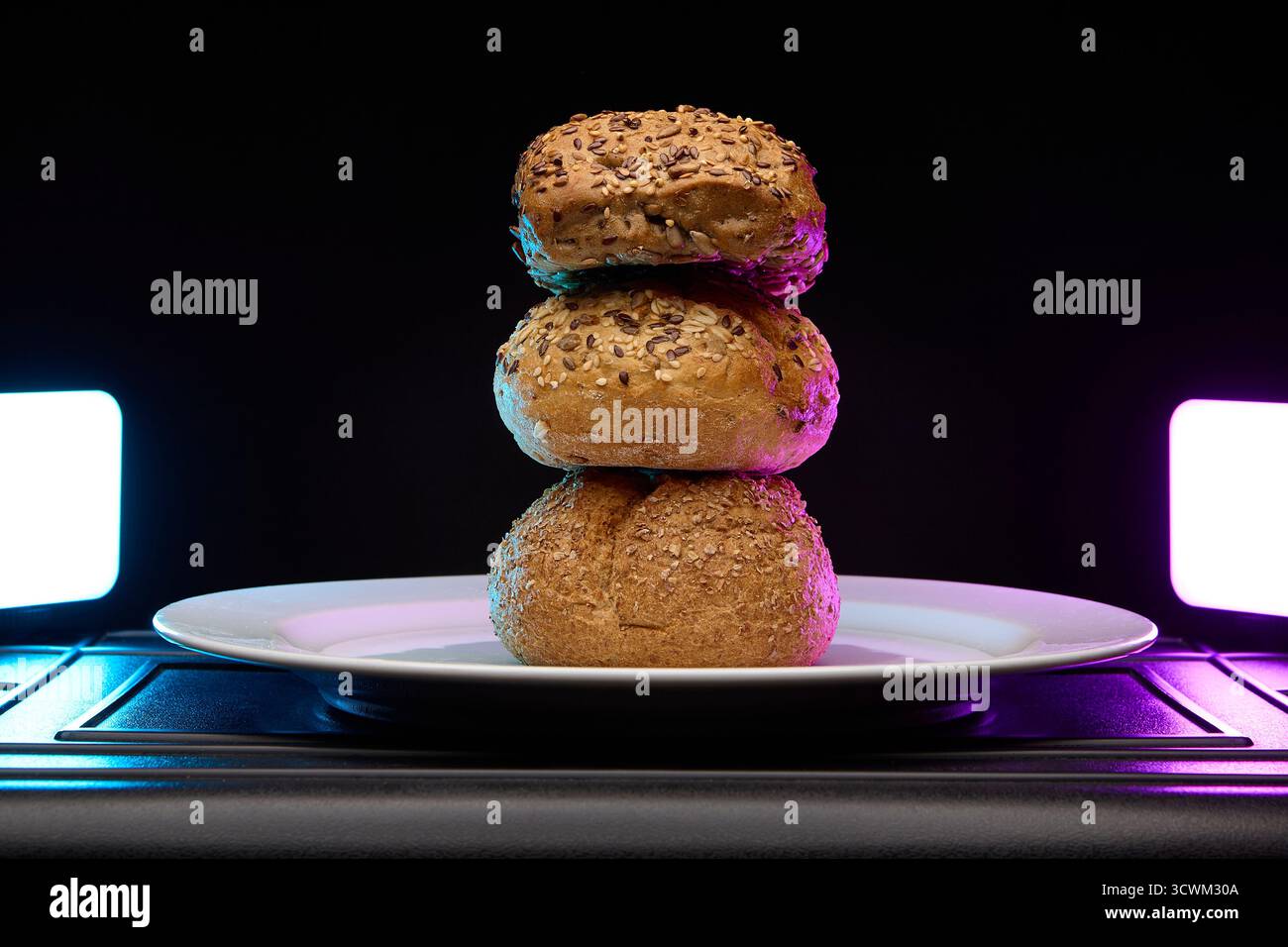 Quatre petits pains empilés les uns sur les autres sous un éclairage créatif de néon violet et cyan. Image conceptuelle de boulangerie pour menus, affiches ou blogs alimentaires. Banque D'Images