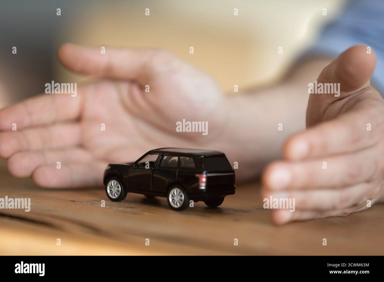 Fermez les mains masculines protégeant le modèle de voiture jouet sur le bureau Banque D'Images