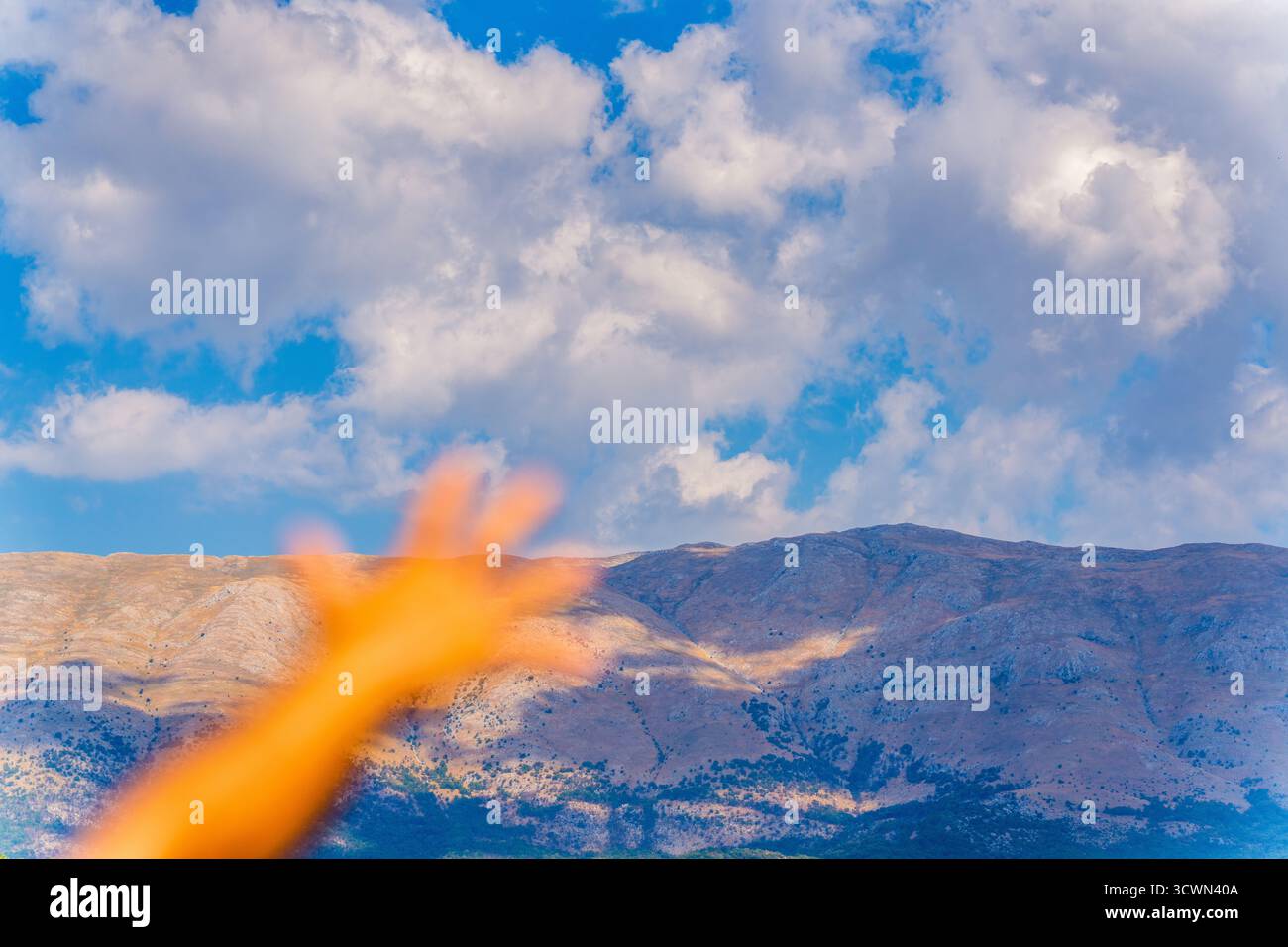 Main floue atteignant vers Majestic Dry Mountain sous Bright Blue Sky et Fluffy White Clouds en Albanie Banque D'Images