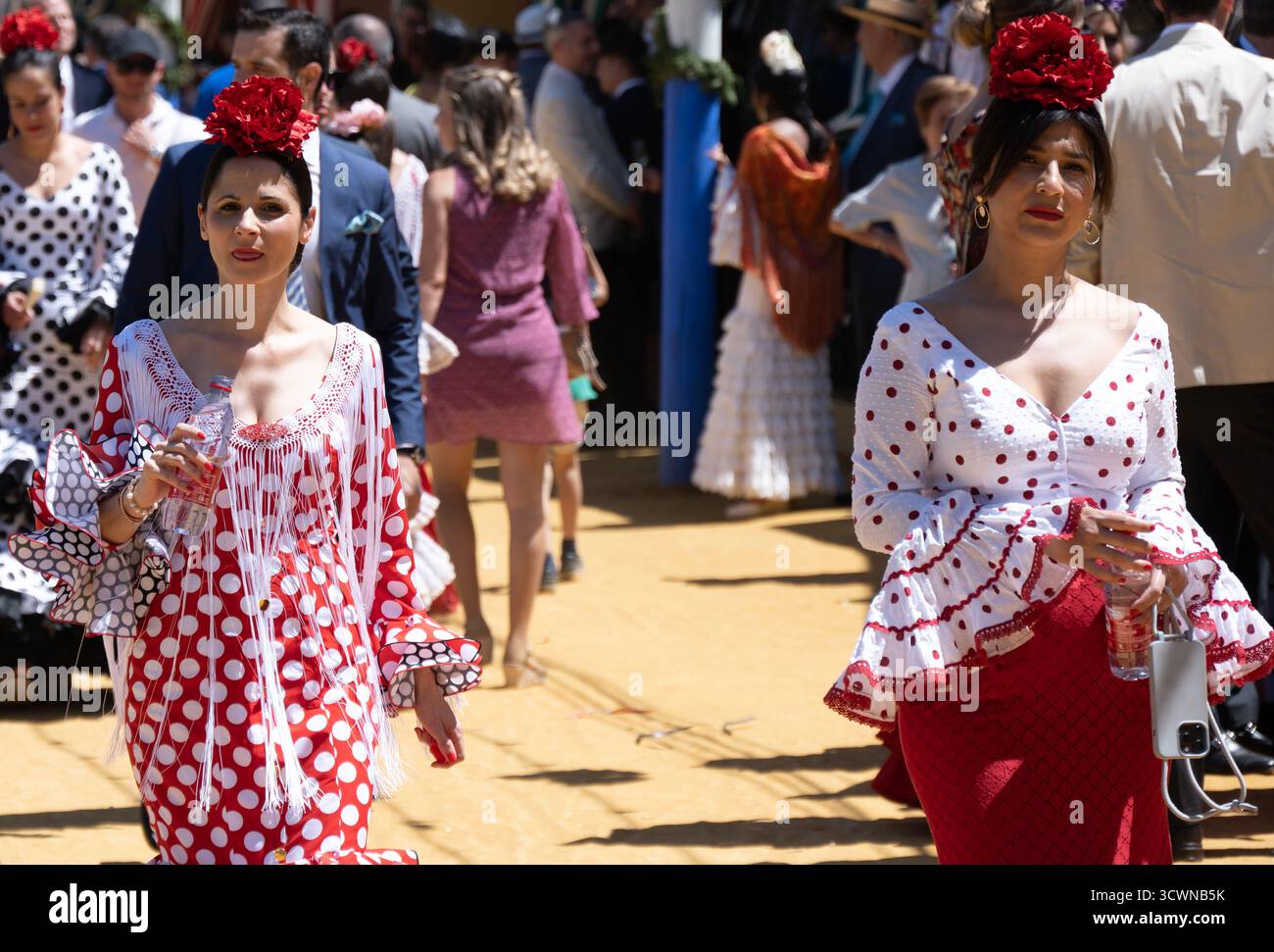 Sevilla, Espagne - 23 avril 23 : deux femmes en robes de flamenco traditionnelles avec pois marchant dans un cadre festif en plein air Banque D'Images