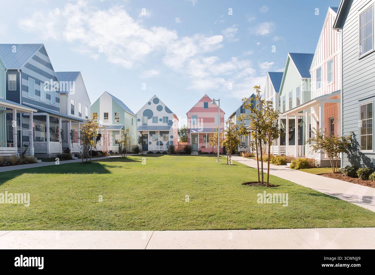 Des maisons aux couleurs pastel bordent une cour herbeuse sous un ciel lumineux. Banque D'Images