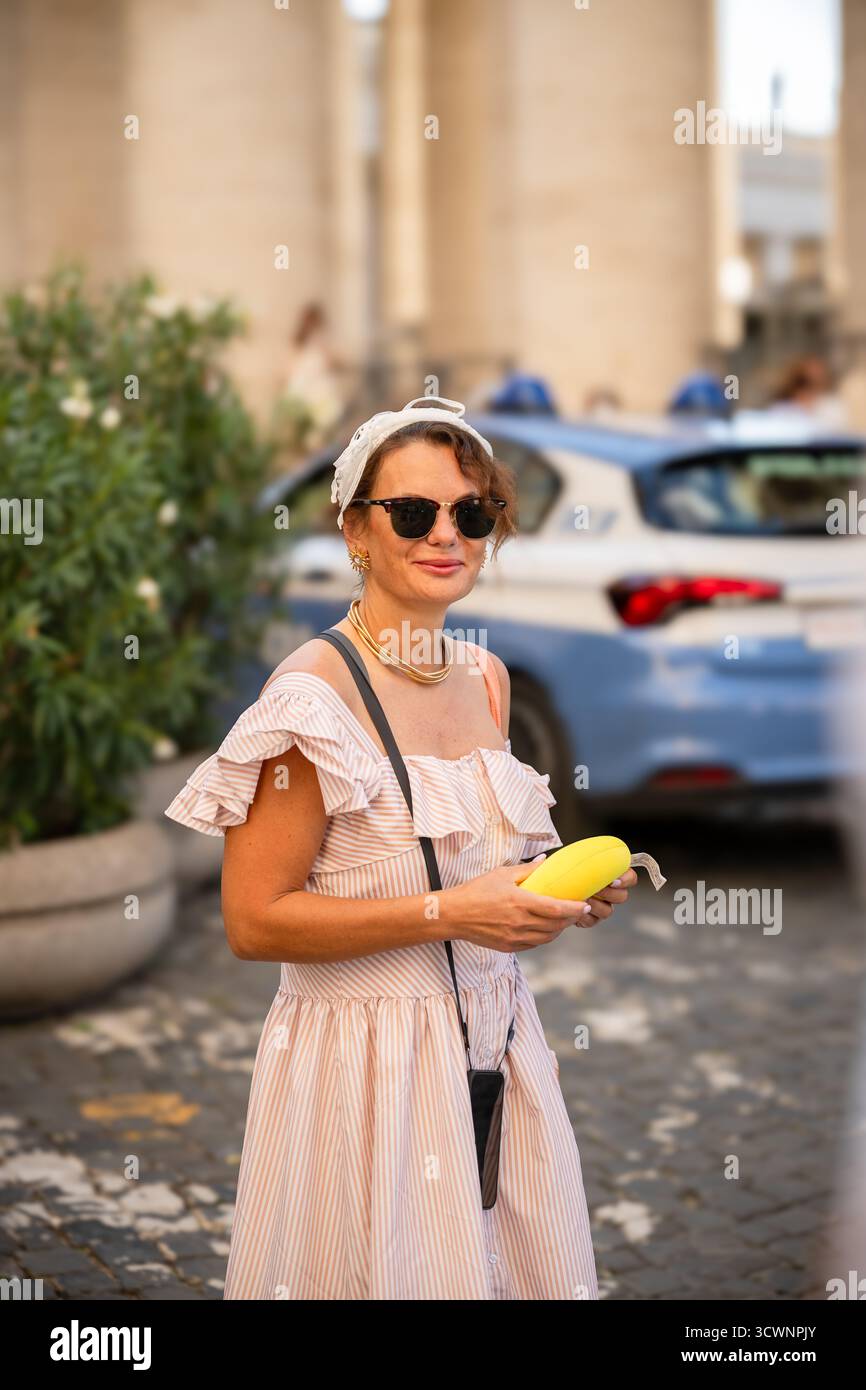 Femme souriante en robe rayée tenant un sac à main jaune sur la rue de la ville Banque D'Images