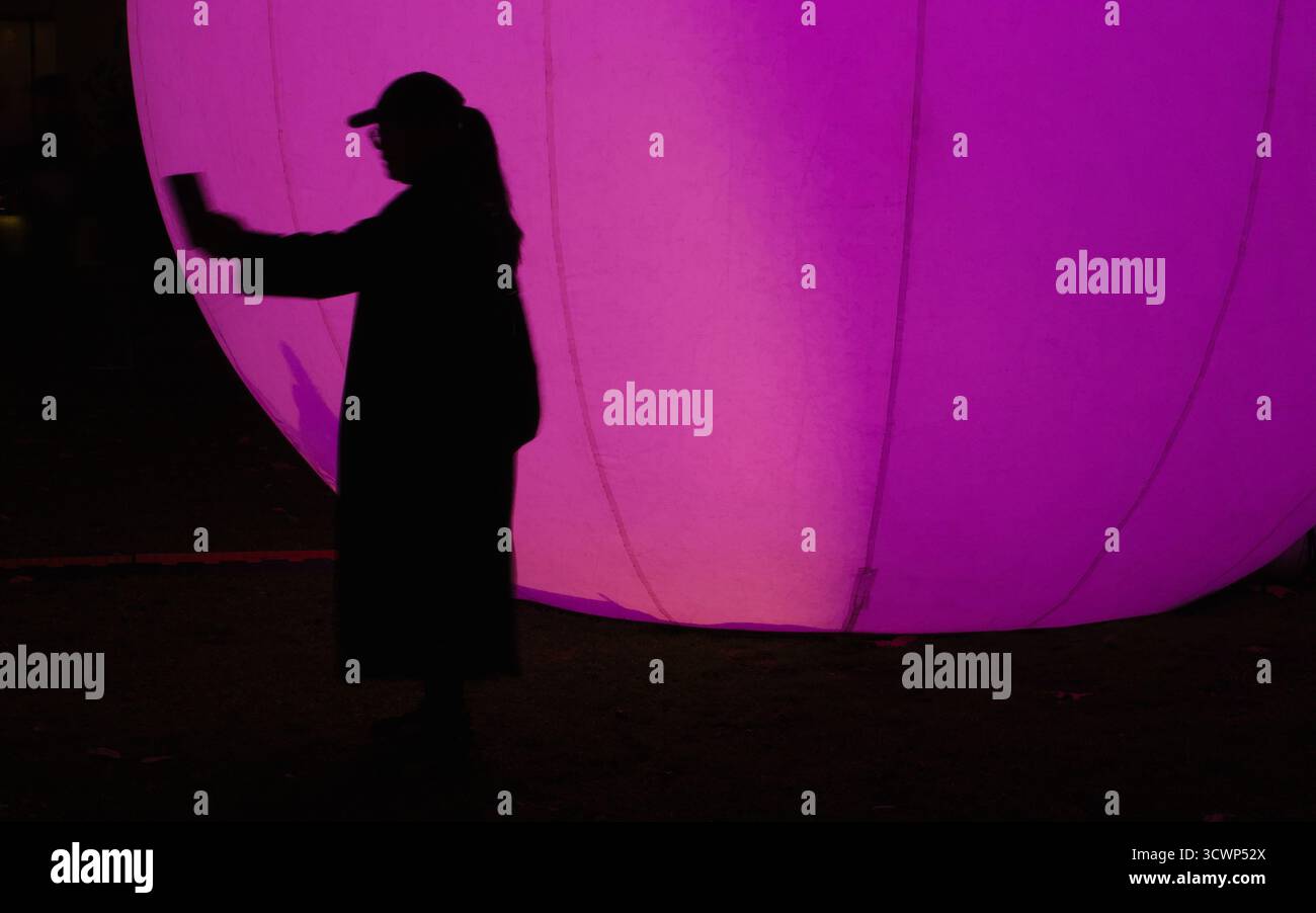Silhouette d'une personne prenant une photo contre un orbe magenta brillant. Moody, contraste dramatique évoquant un sentiment de solitude numérique. Banque D'Images