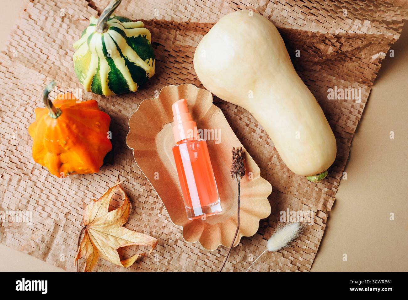 Composition d'automne avec des citrouilles et bouteille cosmétique sur fond de papier artisanal. Soin naturel et concept saisonnier. Vue de dessus, pose à plat. Banque D'Images