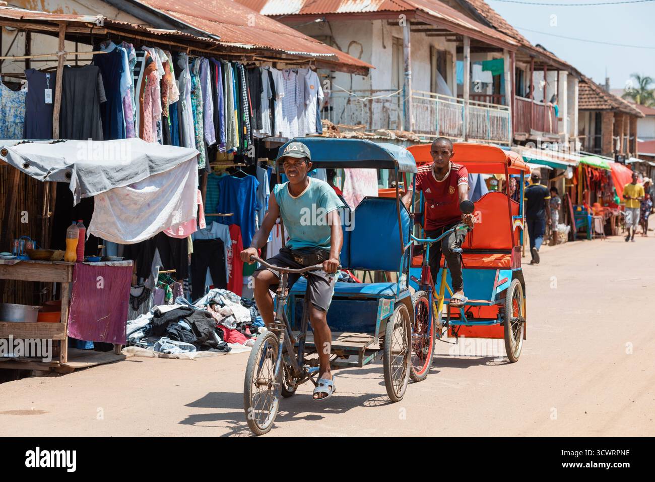 Miandrivazo, Madagascar - 11 octobre 2025 : trajet quotidien à Miandrivazo, montrant les rickshaws à cycle brillamment couverts utilisés pour le transport de passagers. Banque D'Images
