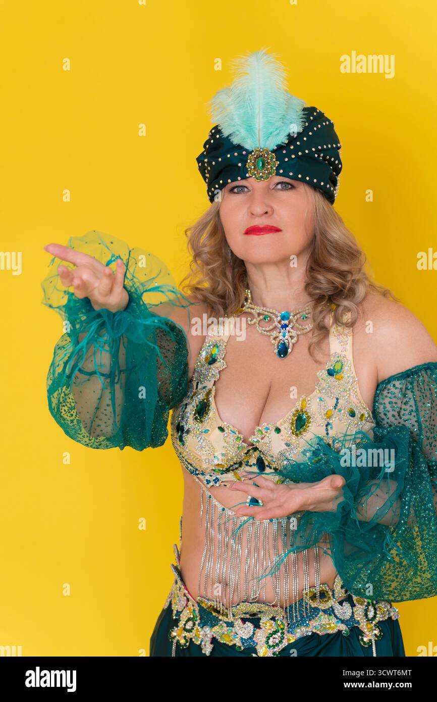 Femme adulte d'âge moyen danseuse exotique regardant la caméra. Mannequin habillant en costume de scène de danse orientale vert jaune - turban, soutien-gorge haut et SK Banque D'Images