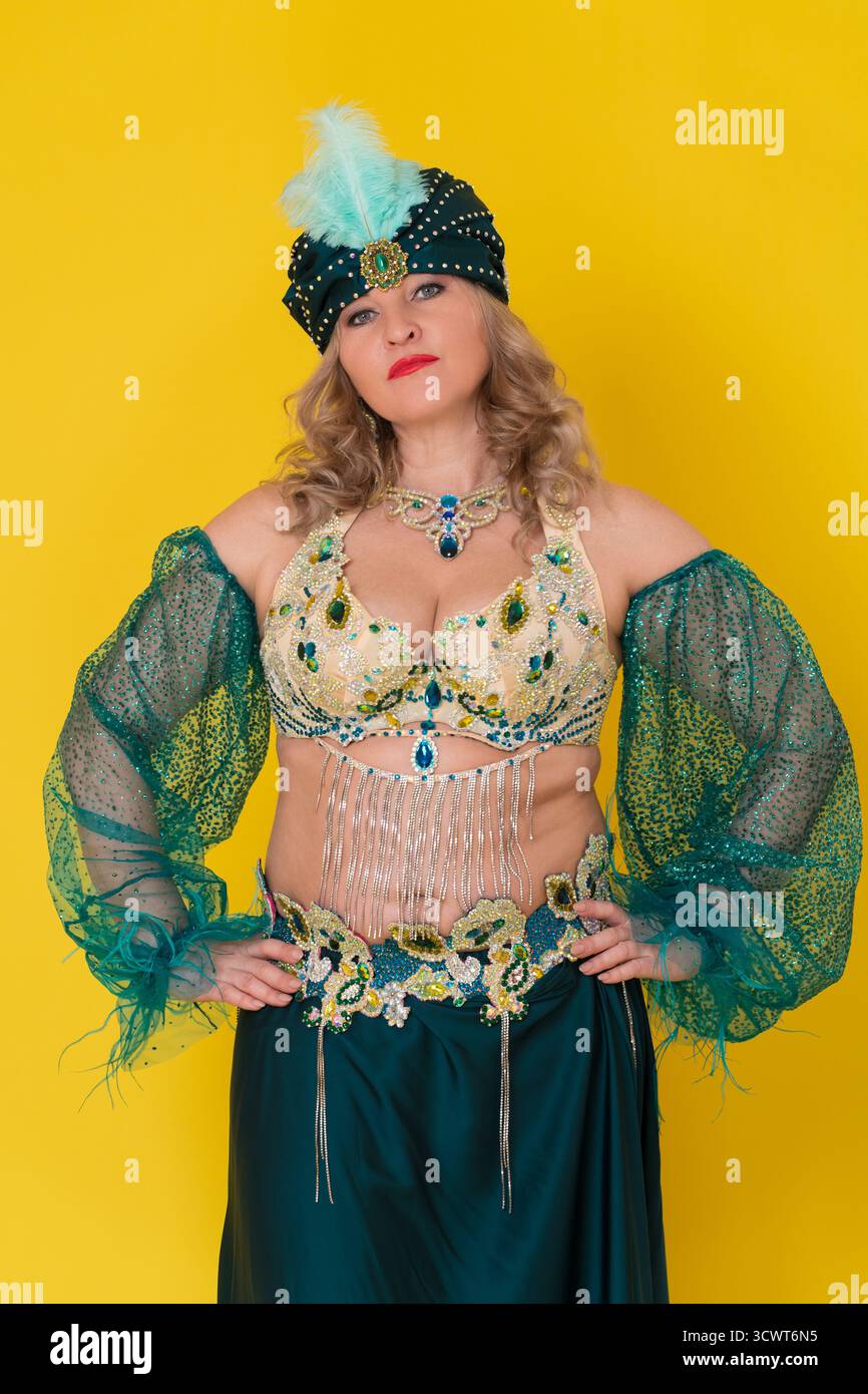 Portrait de modèle de mode femme mature caucasienne avec des bras akimbo vêtus d'une tenue de scène de danse orientale verte - turban, haut de soutien-gorge et jupe, posant agai Banque D'Images
