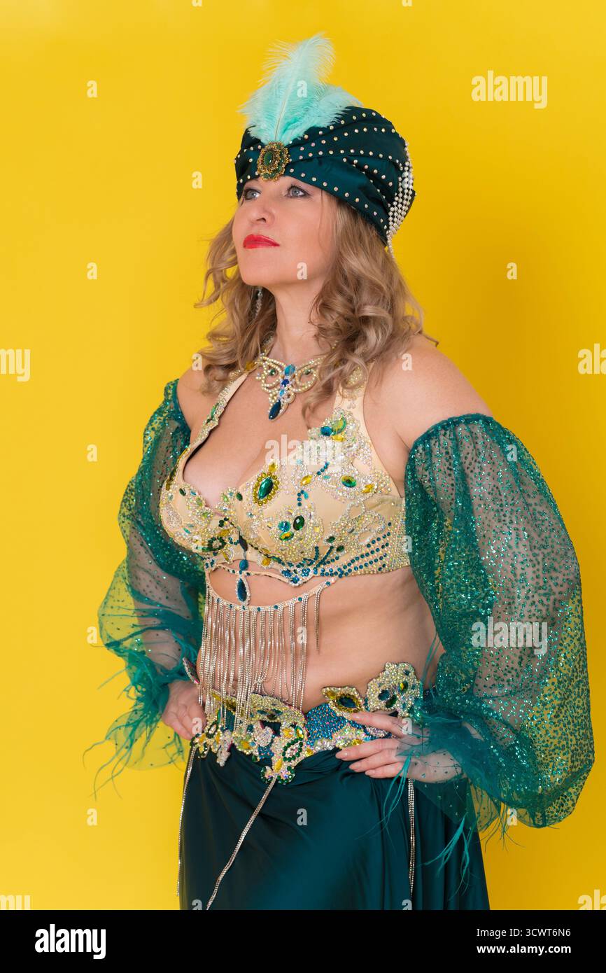 Portrait de sensualité femme modèle de mode avec bras akimbo enfilant dans le vêtement de scène de danse orientale verte - turban, haut de soutien-gorge et jupe, posant contre Banque D'Images