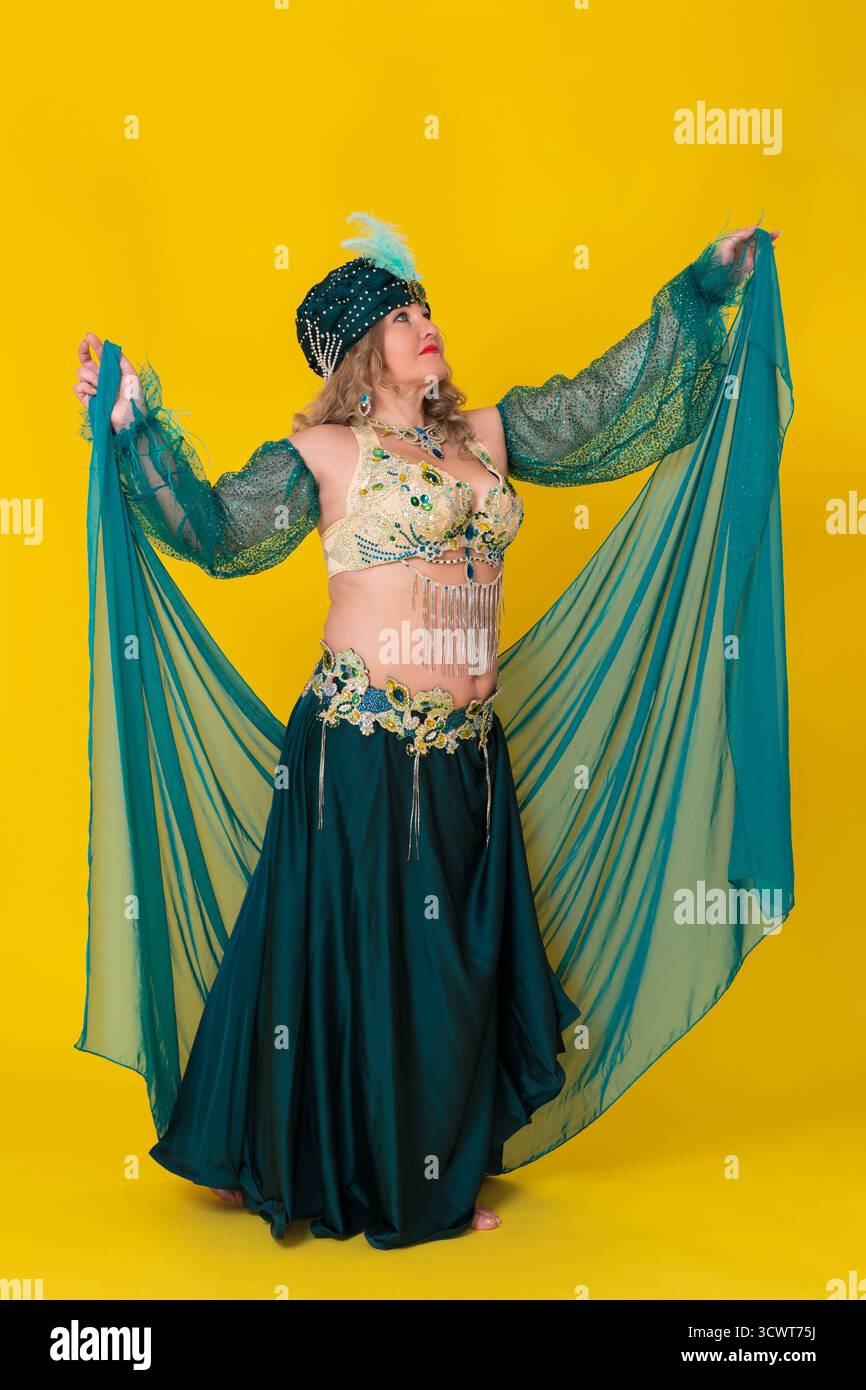 Femme caucasienne danseuse exotique avec les bras tendus vêtus d'une tenue de danse orientale verte - paréo, turban, soutien-gorge, jupe maxi et elle ne porte pas Banque D'Images