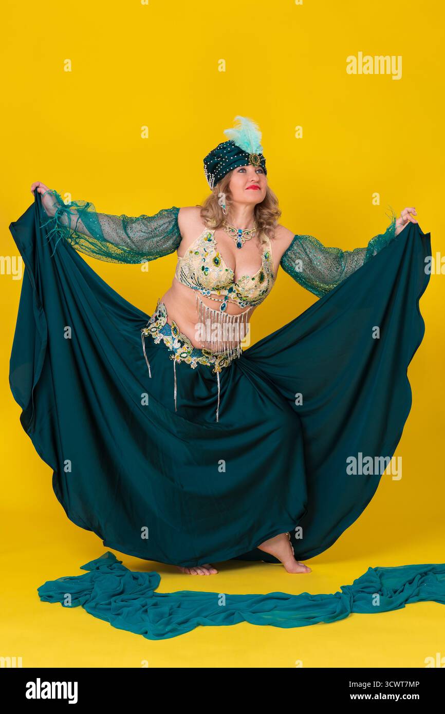 Femme adulte d'âge moyen danseuse du ventre exotique s'habillant dans une tenue de scène de danse orientale verte - turban, haut de soutien-gorge et jupe longue, sans chaussures ou chaussettes, pe Banque D'Images