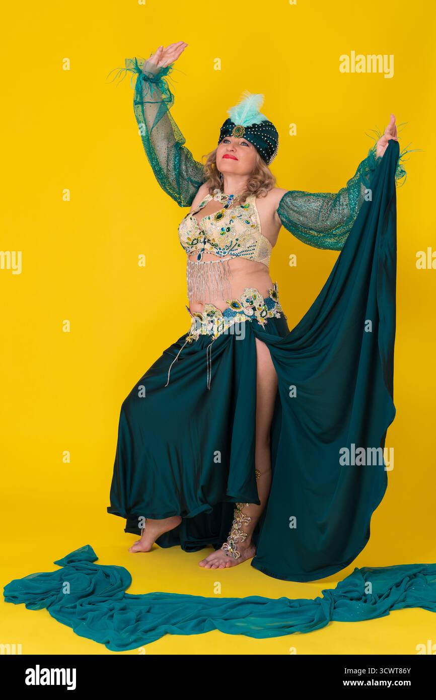 Modèle de mode femme mature heureux avec enfiler à la main dans le costume de scène de danse orientale vert - turban, haut de soutien-gorge et jupe longue avec fente, mouvements et Banque D'Images