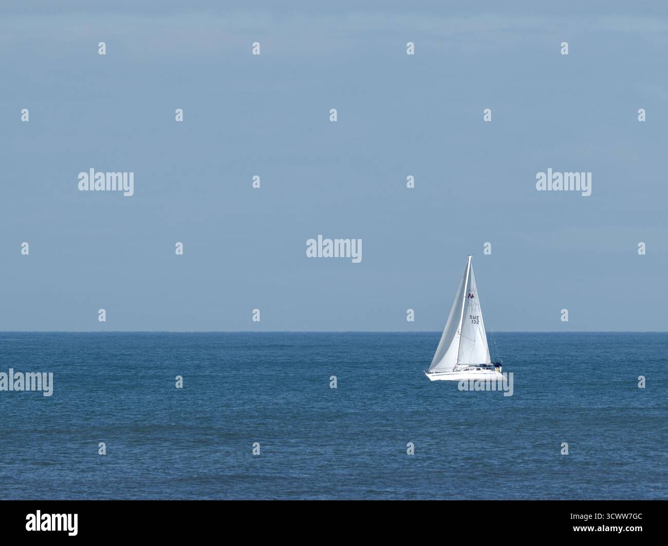Voilier avec voiles blanches sur l'océan bleu calme sous ciel clair symbolisant la liberté et la sérénité Banque D'Images