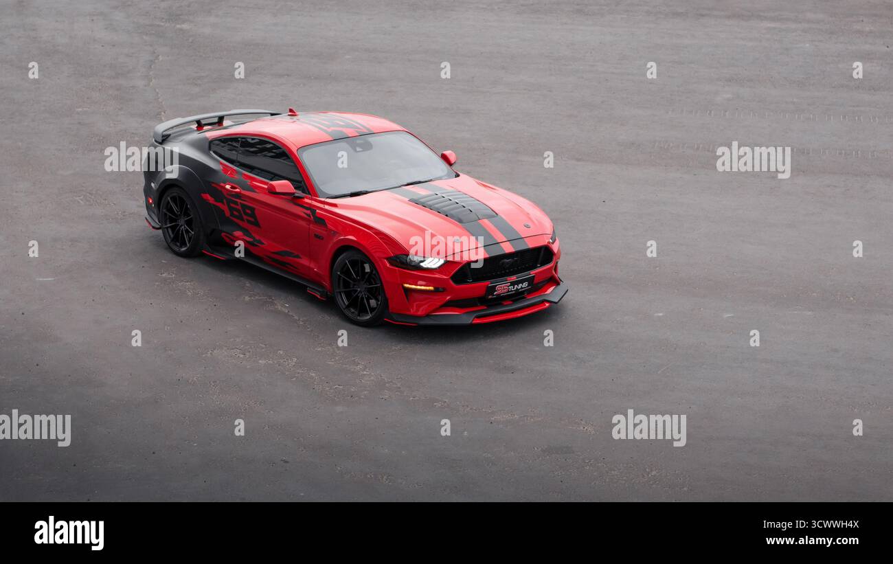 Red Ford Mustang dans le parking au crépuscule. Vue aérienne de trois quarts de face d'un poney américain garé sur un immense champ d'asphalte vide. Banque D'Images