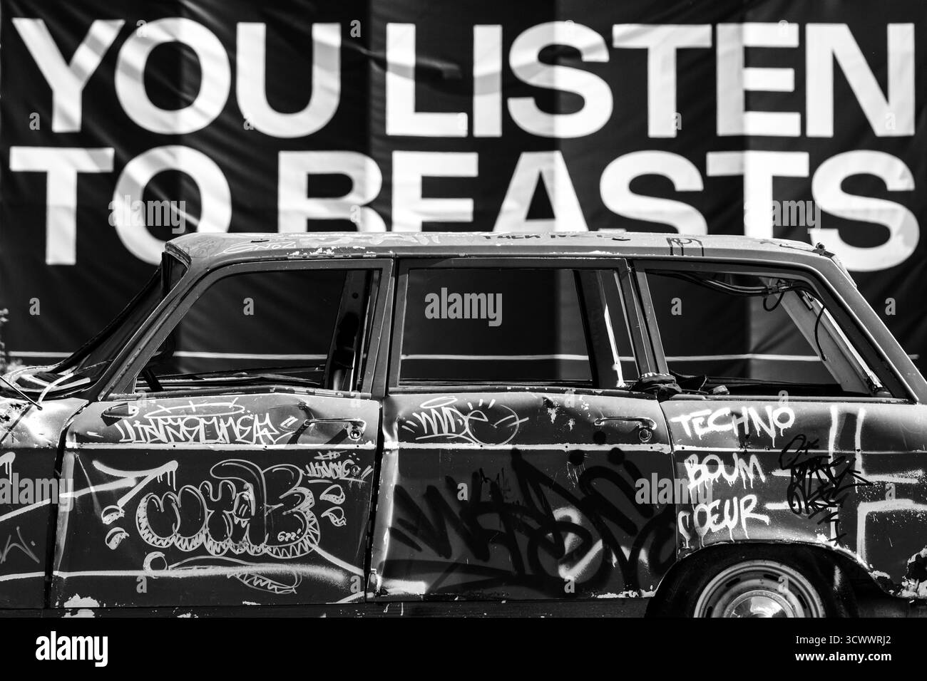 Voiture abandonnée couverte de graffiti dans un cadre urbain avec Street Art et Billboard Text - scène urbaine contemporaine Banque D'Images