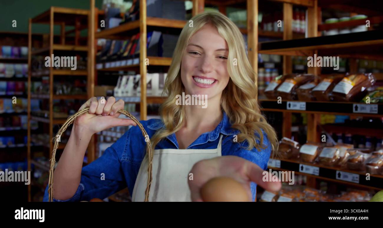Employé du magasin portant un tablier léger offrant des œufs frais à l'épicerie, avec un panier en osier près des étagères Banque D'Images