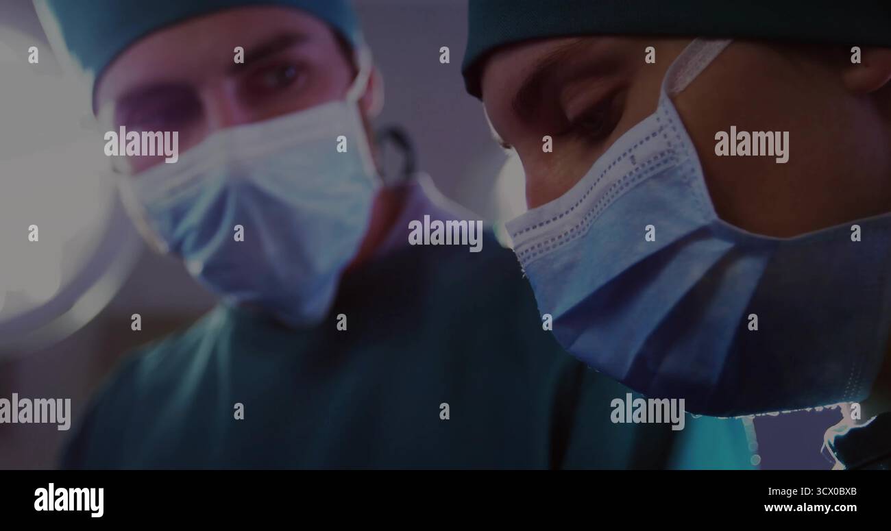 Chirurgien féminin penché portant des gommages verts masques les capuchons sous la lampe dans OU, avec collègue flou Banque D'Images