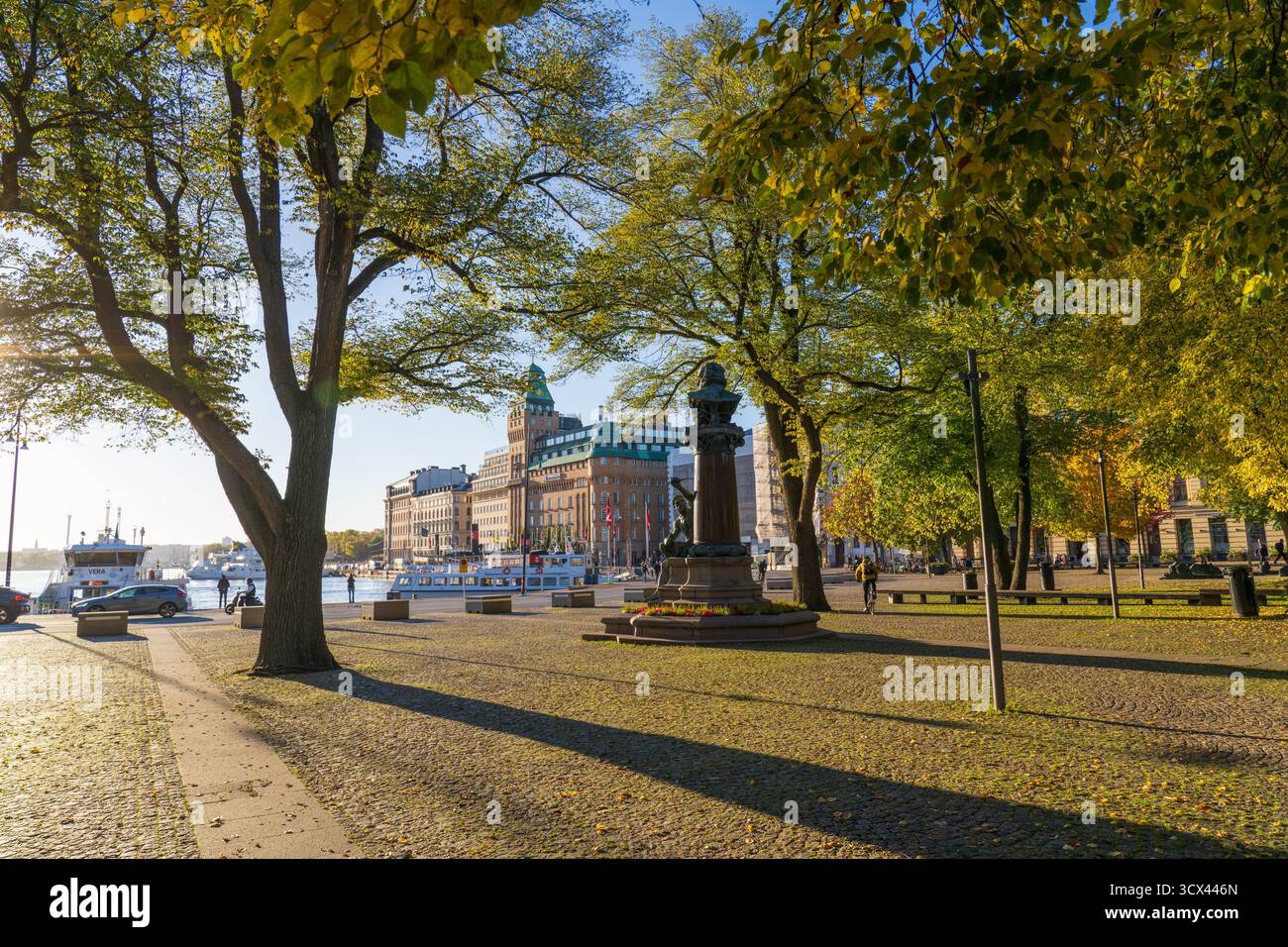 Vue panoramique automnale d’un monument-fontaine historique sur une place ensoleillée à Stockholm, Suède, encadrée d’arbres verts et jaunes Banque D'Images