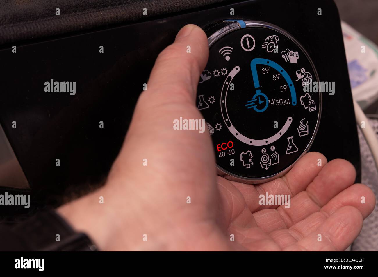 Gros plan de la main d’un homme tournant le thermostat d’une machine à laver en mode éco. Concept d'économie d'énergie et d'eau en raison de l'augmentation des cos de service public Banque D'Images