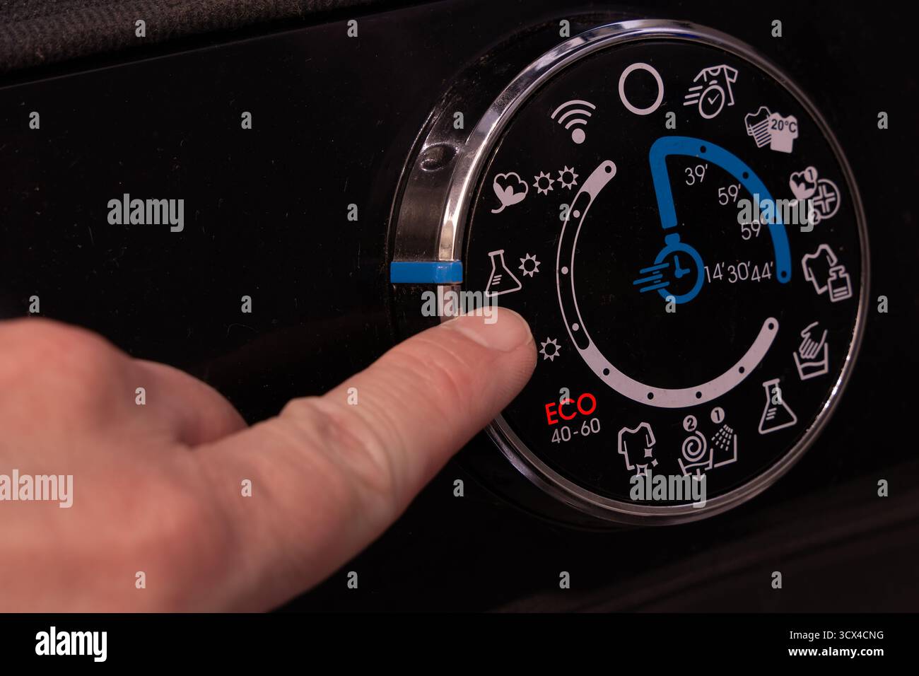 Gros plan de la main d’un homme tournant le thermostat d’une machine à laver en mode éco. Concept d'économie d'énergie et d'eau en raison de l'augmentation des cos de service public Banque D'Images