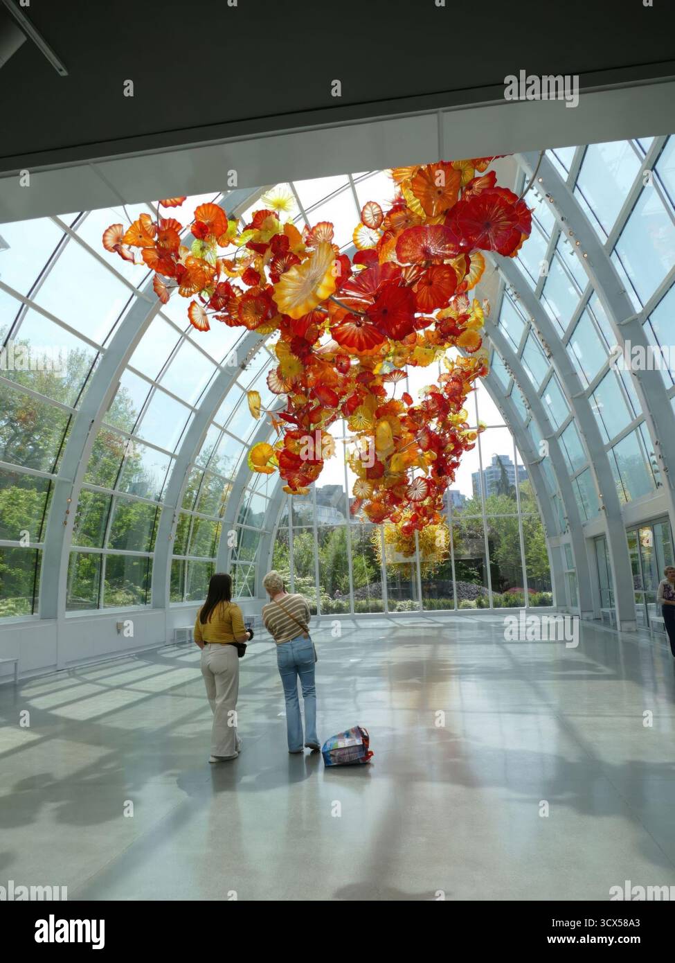 SEATTLE - APR 25, 2025 - deux femmes regardent une grande sculpture en verre coloré de Dale Chihuly suspendue au plafond d'un moderne et lumineux Banque D'Images