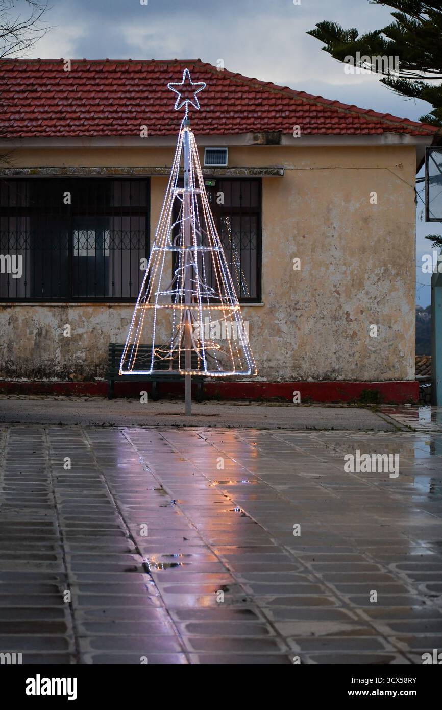 Installation lumineuse festive de sapin de Noël debout sur une place rustique de village européen. La lueur brillante de la décoration de vacances reflète magnifiquement sur t Banque D'Images