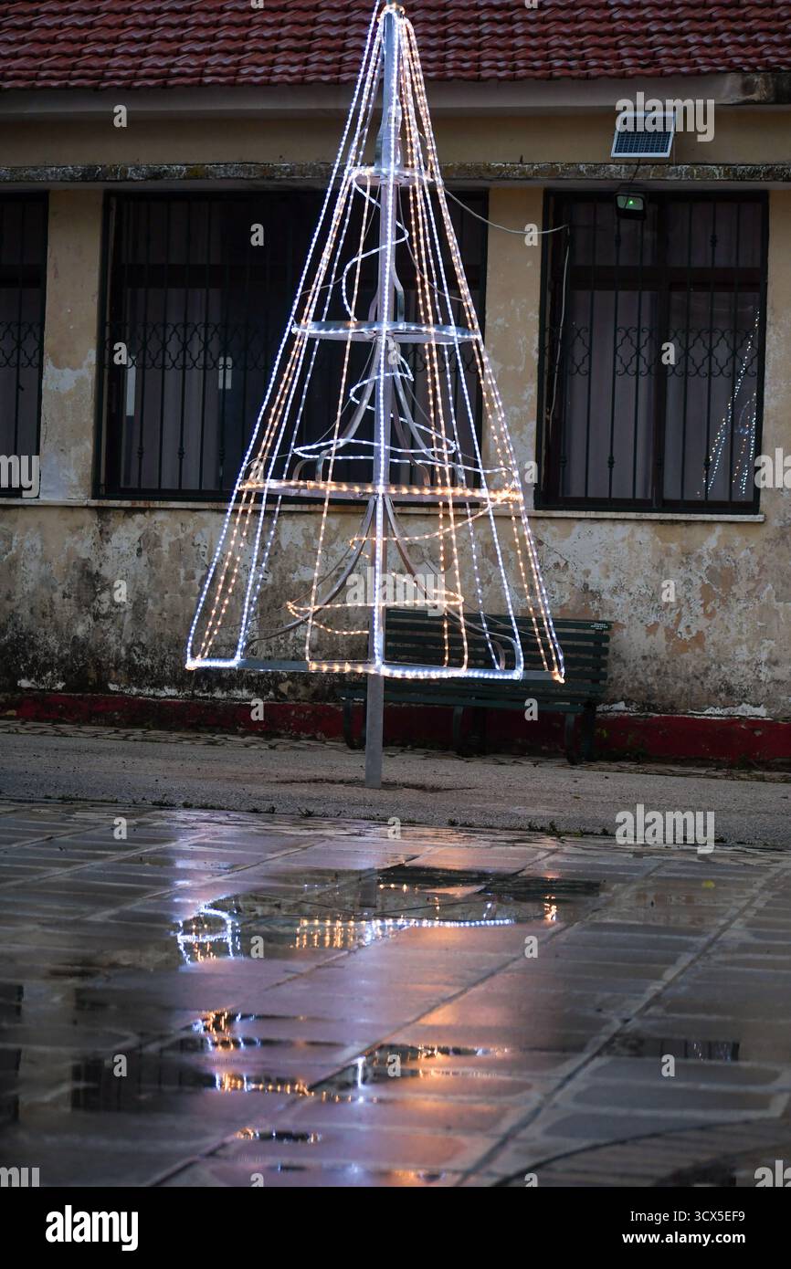 Décoration lumineuse de sapin de Noël avec une étoile sur le dessus, magnifiquement reflété dans une flaque sur le trottoir humide de la ville au crépuscule. Des vacances festives en plein air Banque D'Images