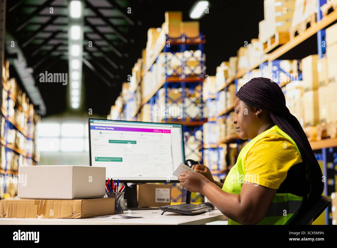 Femme afro-américaine manipulant l'étiquetage avec les détails de l'expédition étiquettes adhésives, travaillant sur le traitement des commandes et préparant les détails de l'expédition pour la distribution. Centre de distribution e-commerce. Banque D'Images
