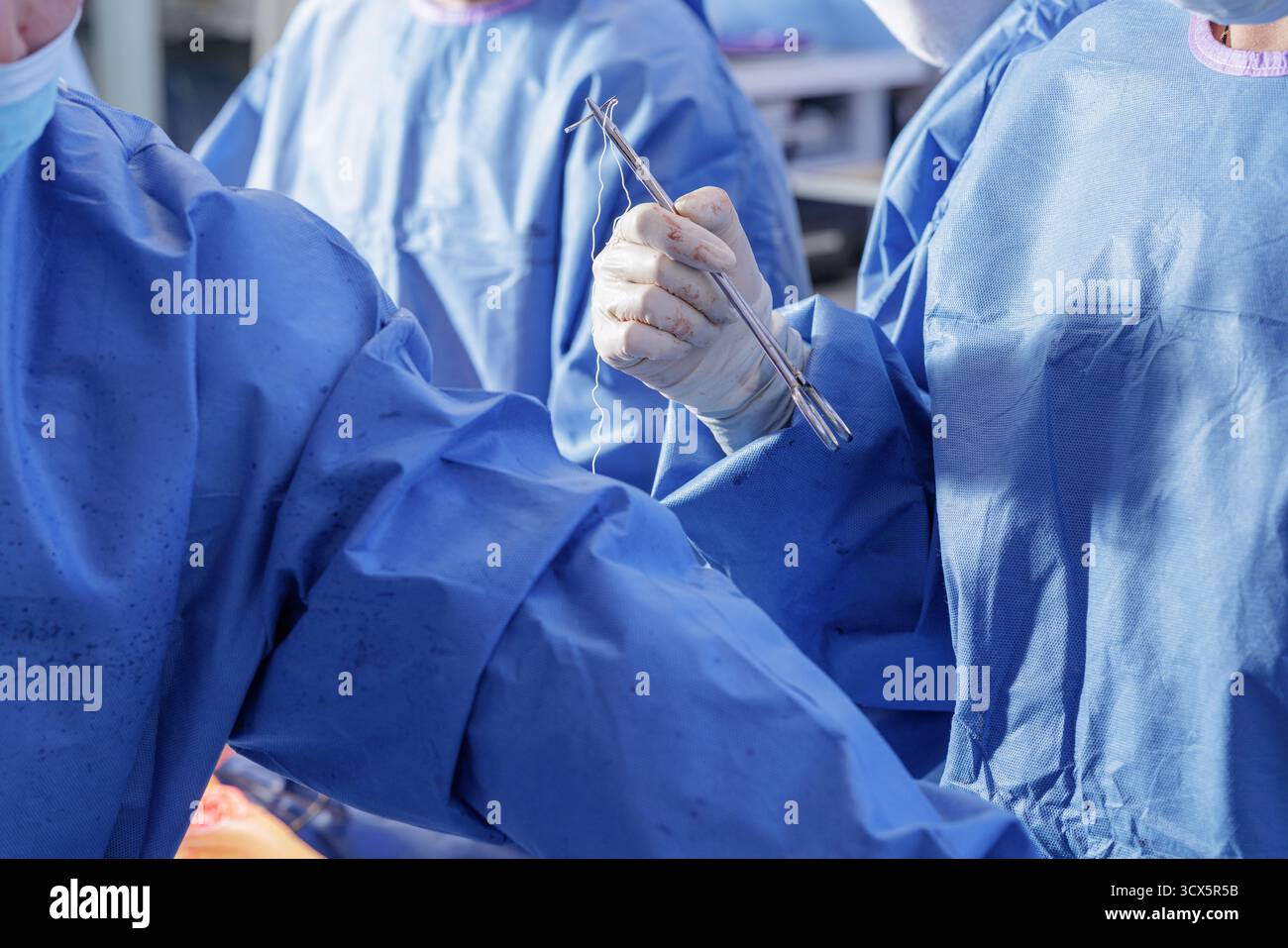 Le chirurgien ganté saisit un tournevis d'aiguille avec fil lors de la fermeture de la plaie dans une salle d'opération orthopédique stérile, idéal pour la formation médicale et éditoriale Banque D'Images